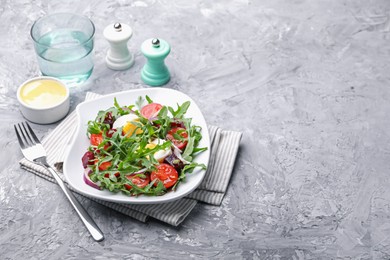 Photo of Tasty salad with arugula, vegetables and egg served on grey table, space for text