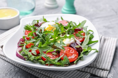 Photo of Tasty salad with arugula, vegetables, egg and seeds on grey table, closeup