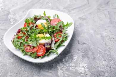 Photo of Tasty salad with arugula, vegetables, egg and seeds on grey table, closeup. Space for text