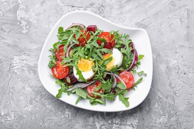 Photo of Tasty salad with arugula, vegetables, egg and seeds on grey table, top view