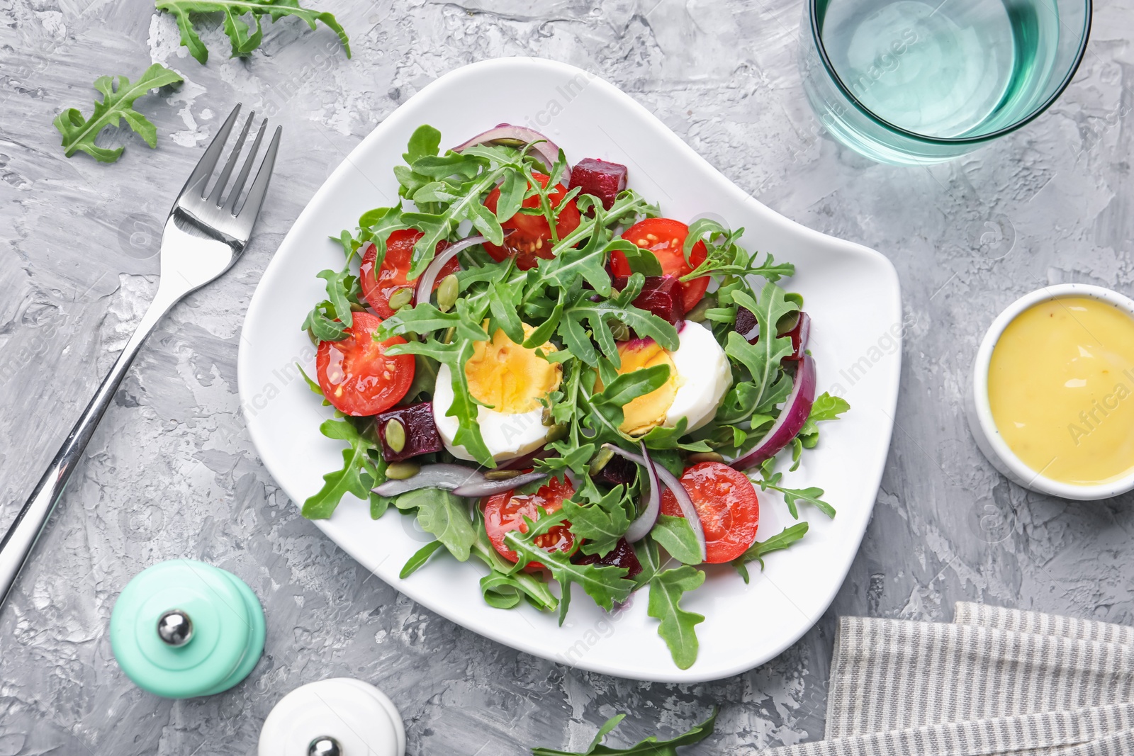 Photo of Tasty salad with arugula, vegetables and egg served on grey table, flat lay