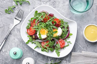Photo of Tasty salad with arugula, vegetables and egg served on grey table, flat lay