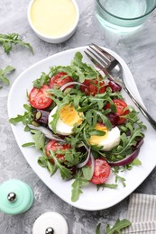 Photo of Tasty salad with arugula, vegetables and egg served on grey table, flat lay
