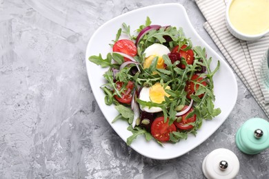 Photo of Tasty salad with arugula, vegetables and egg served on grey table, flat lay. Space for text