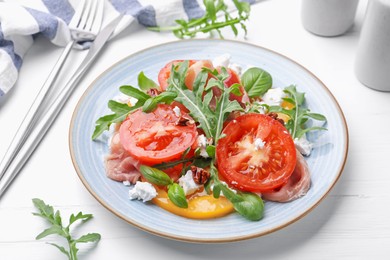 Photo of Tasty salad with arugula, cheese, tomatoes, nuts and prosciutto on white wooden table, closeup