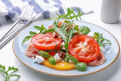 Photo of Tasty salad with arugula, cheese, tomatoes, nuts and prosciutto on white wooden table, closeup
