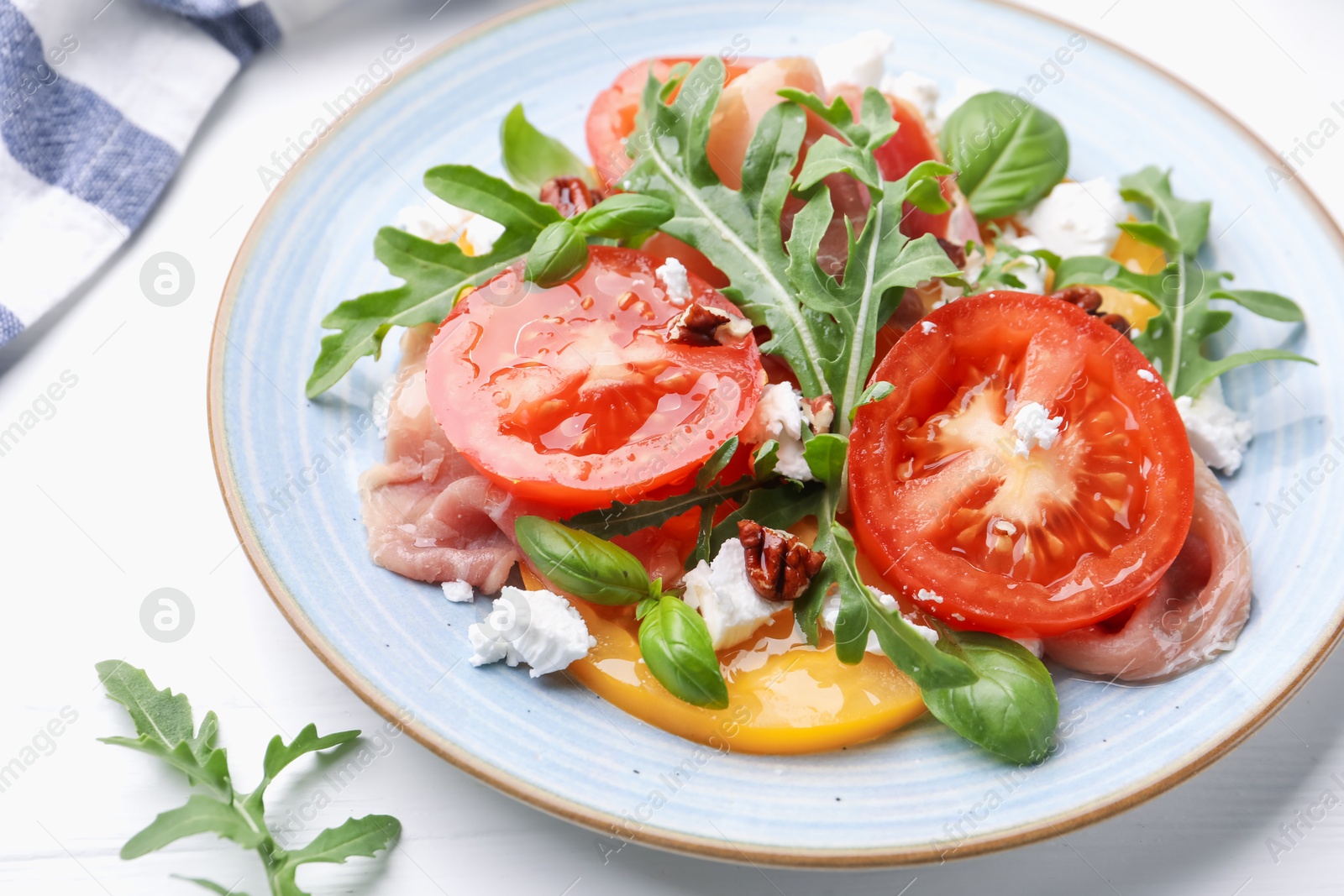 Photo of Tasty salad with arugula, cheese, tomatoes, nuts and prosciutto on white wooden table, closeup