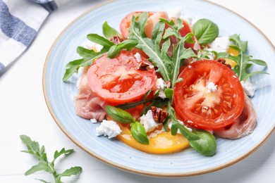 Photo of Tasty salad with arugula, cheese, tomatoes, nuts and prosciutto on white wooden table, closeup
