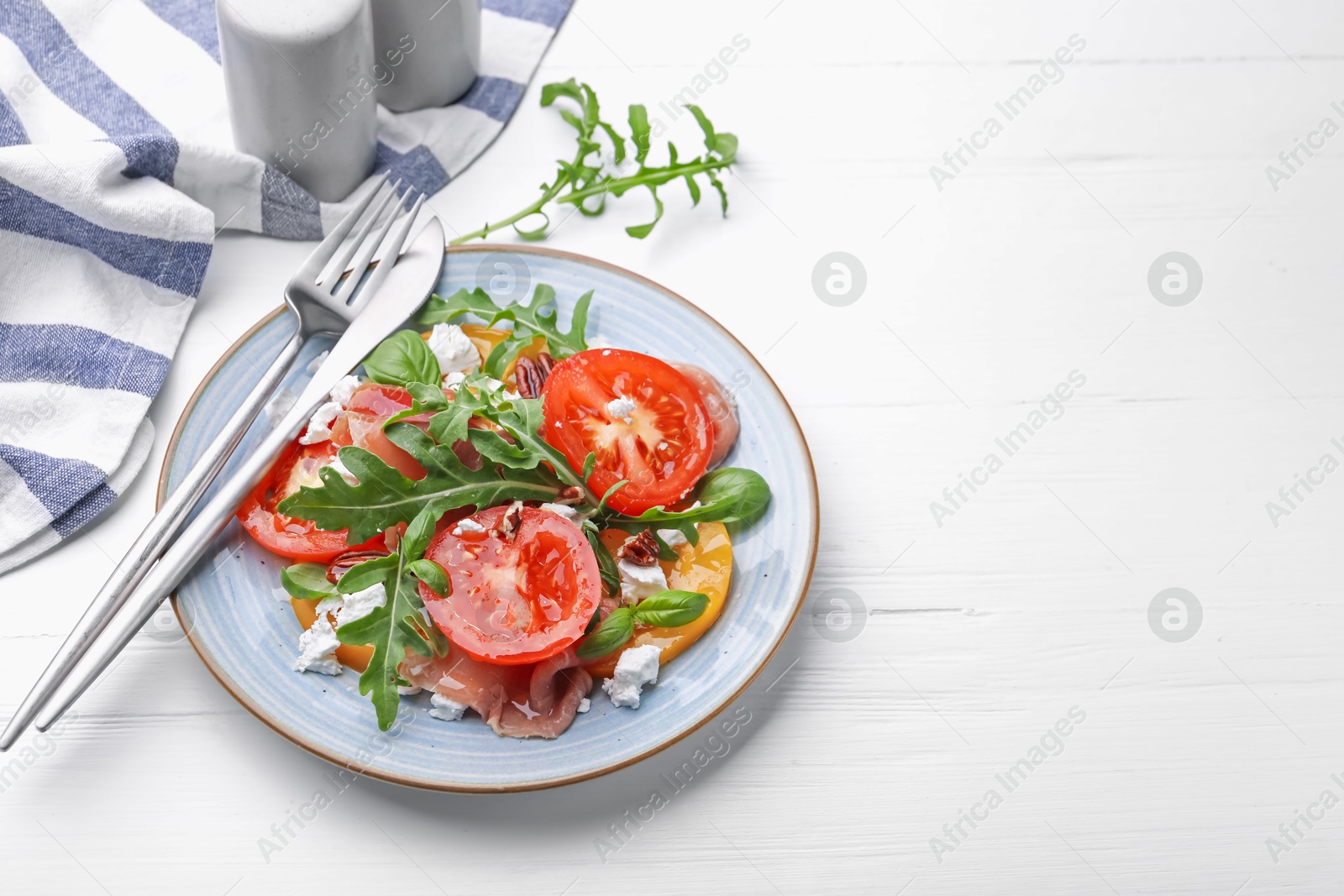 Photo of Tasty salad with arugula, cheese, tomatoes, nuts and prosciutto on white wooden table, closeup. Space for text