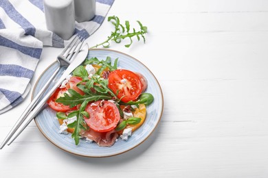 Photo of Tasty salad with arugula, cheese, tomatoes, nuts and prosciutto on white wooden table, closeup. Space for text