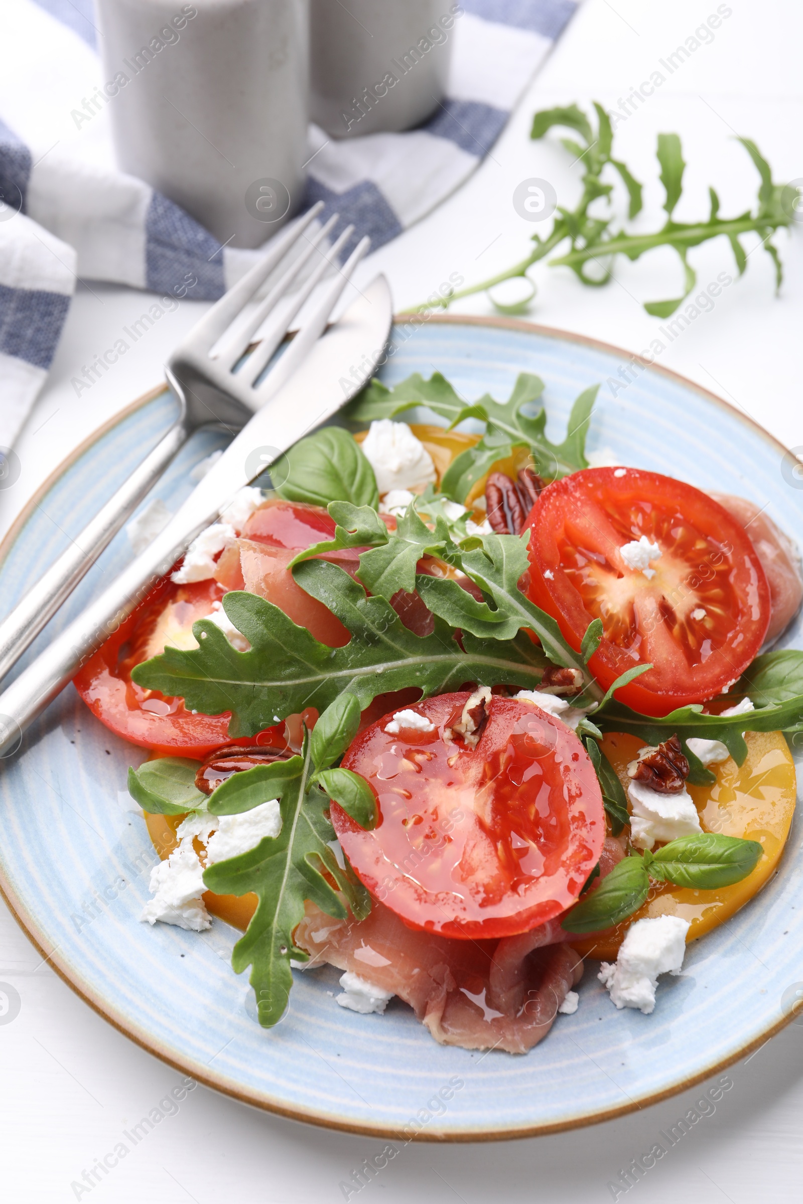 Photo of Tasty salad with arugula, cheese, tomatoes, nuts and prosciutto on white table, closeup