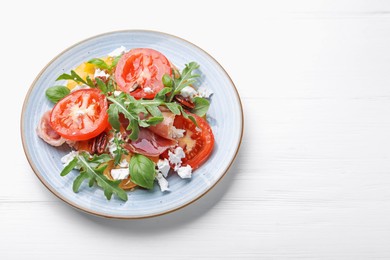Photo of Tasty salad with arugula, cheese, tomatoes, nuts and prosciutto on white wooden table, above view. Space for text