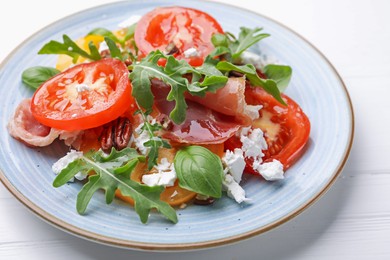 Photo of Tasty salad with arugula, cheese, tomatoes, nuts and prosciutto on white wooden table, closeup