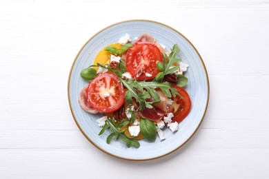 Photo of Tasty salad with arugula, cheese, tomatoes, nuts and prosciutto on white wooden table, top view