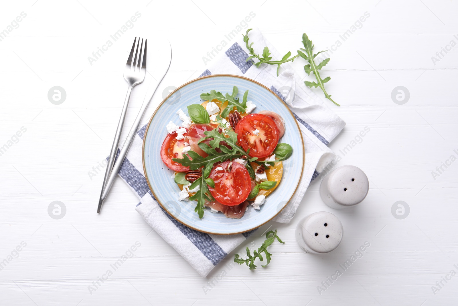 Photo of Tasty salad with arugula, cheese, tomatoes, nuts and prosciutto on white wooden table, flat lay