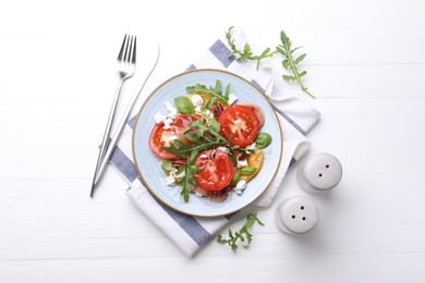 Photo of Tasty salad with arugula, cheese, tomatoes, nuts and prosciutto on white wooden table, flat lay