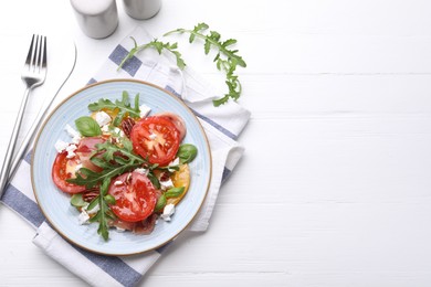 Photo of Tasty salad with arugula, cheese, tomatoes, nuts and prosciutto on white wooden table, flat lay. Space for text