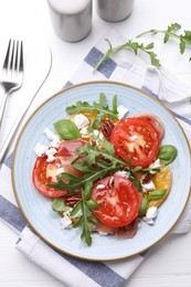 Photo of Tasty salad with arugula, cheese, tomatoes, nuts and prosciutto on white wooden table, flat lay