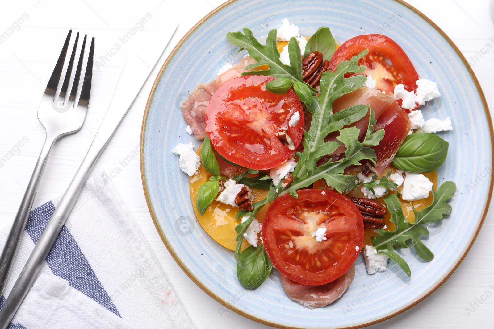 Photo of Tasty salad with arugula, cheese, tomatoes, nuts and prosciutto on white wooden table, flat lay