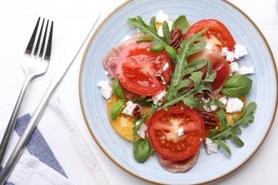 Photo of Tasty salad with arugula, cheese, tomatoes, nuts and prosciutto on white wooden table, flat lay