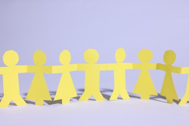 Photo of Paper figures of people holding hands on white background, closeup