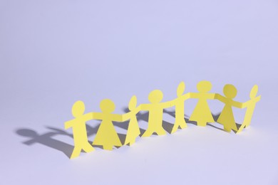 Photo of Paper figures of people holding hands on white background, closeup