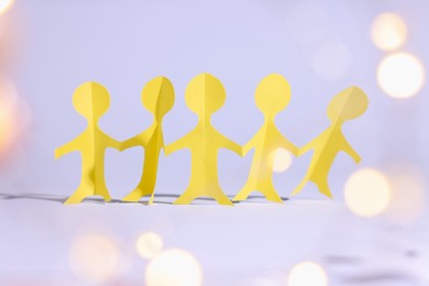 Photo of Paper figures of people holding hands on white background, bokeh effect