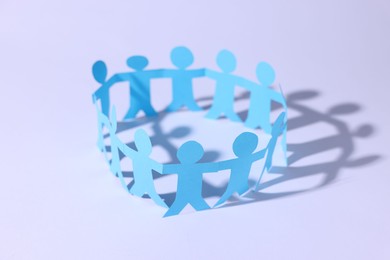 Photo of Paper figures of people holding hands on white background, closeup