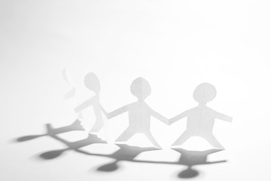 Photo of Paper figures of people holding hands on white background, closeup
