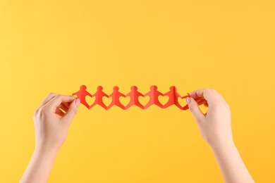 Photo of Woman holding paper figures of people on orange background, closeup