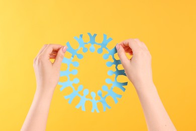 Photo of Woman holding paper figures of people on orange background, closeup