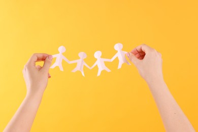Photo of Woman holding paper figures of people on orange background, closeup