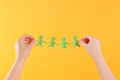 Photo of Woman holding paper figures of people on orange background, closeup