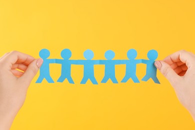 Photo of Woman holding paper figures of people on orange background, closeup