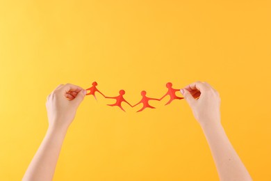 Photo of Woman holding paper figures of people on orange background, closeup