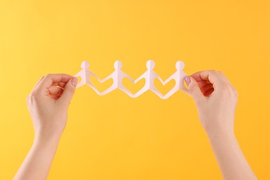 Photo of Woman holding paper figures of people on orange background, closeup