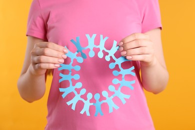 Photo of Woman holding paper figures of people on orange background, closeup