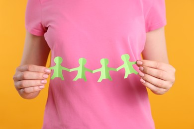 Photo of Woman holding paper figures of people on orange background, closeup