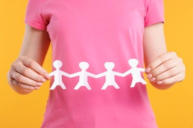 Photo of Woman holding paper figures of people on orange background, closeup