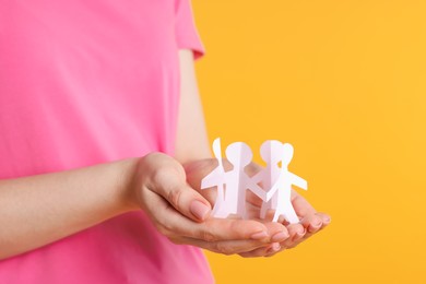 Photo of Woman holding paper figures of people on orange background, closeup
