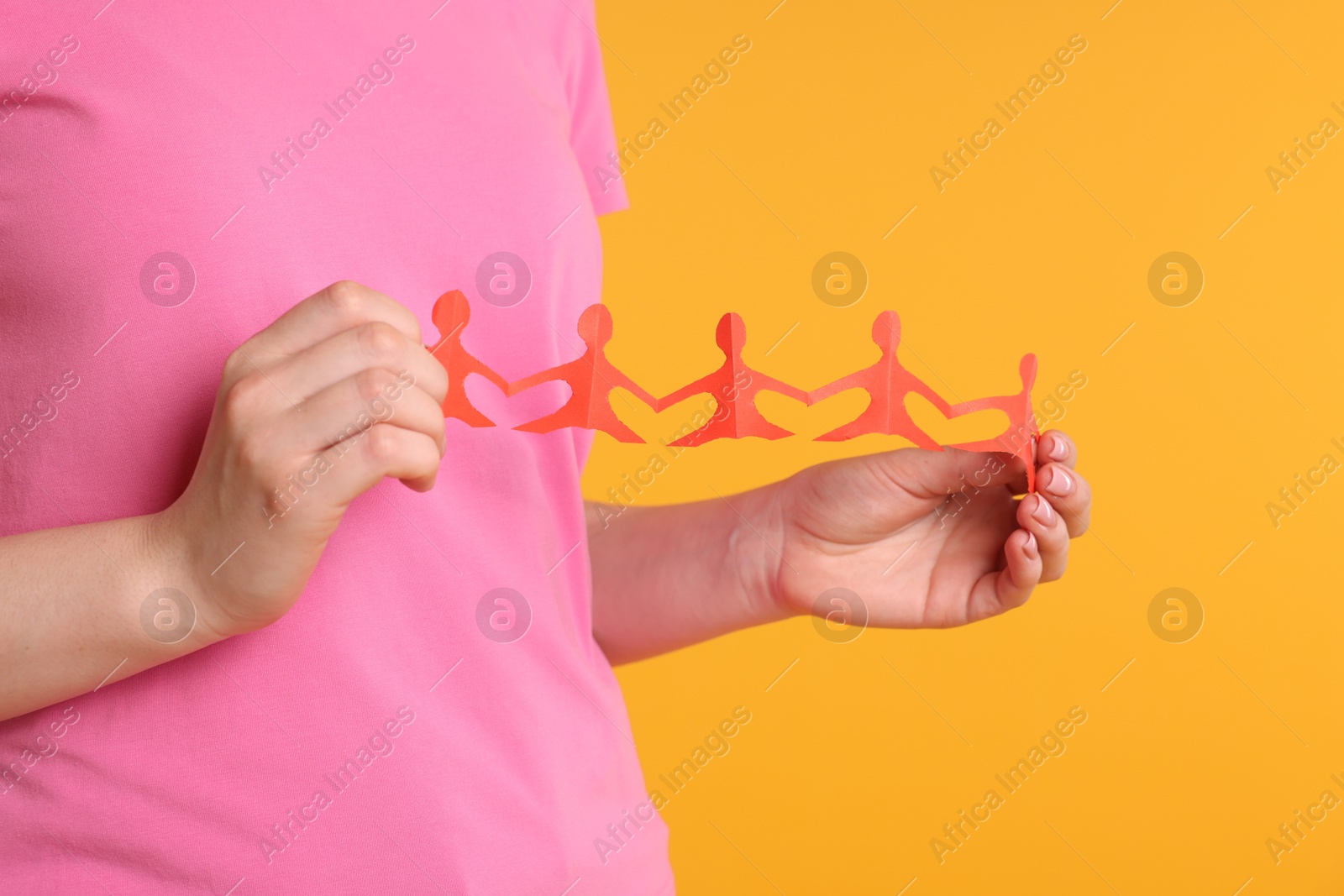 Woman holding paper figures of people on orange background, closeup Photo of Woman holding paper figures of people on orange background, closeup