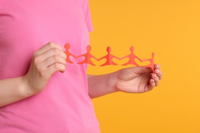 Photo of Woman holding paper figures of people on orange background, closeup