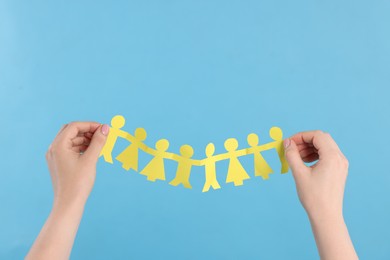 Photo of Woman holding paper figures of people on light blue background, closeup