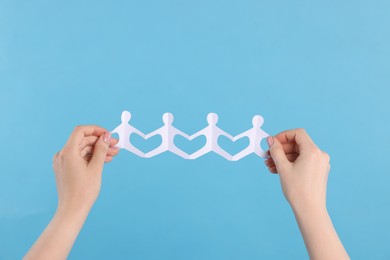 Photo of Woman holding paper figures of people on light blue background, closeup