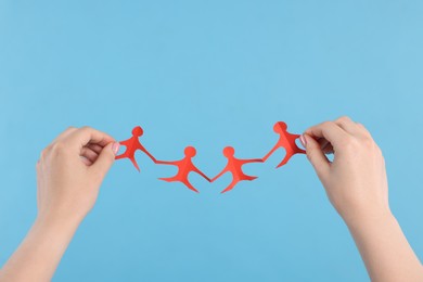 Photo of Woman holding paper figures of people on light blue background, closeup