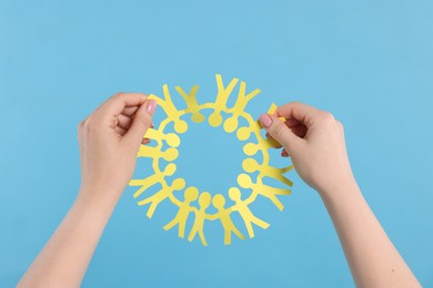 Photo of Woman holding paper figures of people on light blue background, closeup