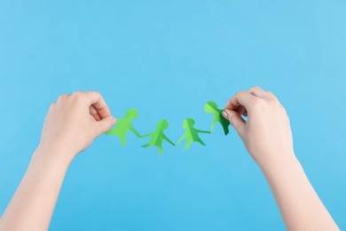 Photo of Woman holding paper figures of people on light blue background, closeup