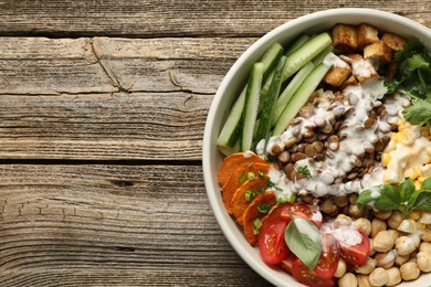 Photo of Healthy vegetarian food. Delicious Buddha bowl with lentils, tofu, chickpeas, vegetables and sauce on wooden table, top view. Space for text