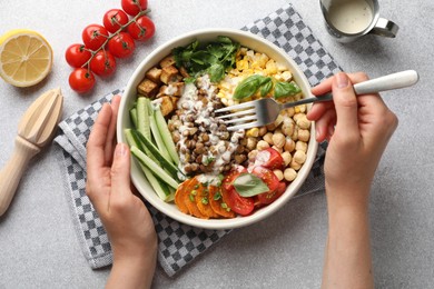 Photo of Healthy vegetarian food. Woman eating delicious Buddha bowl at light grey table, top view