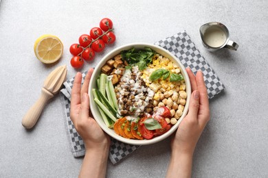 Photo of Healthy vegetarian food. Woman with delicious Buddha bowl at light grey table, top view